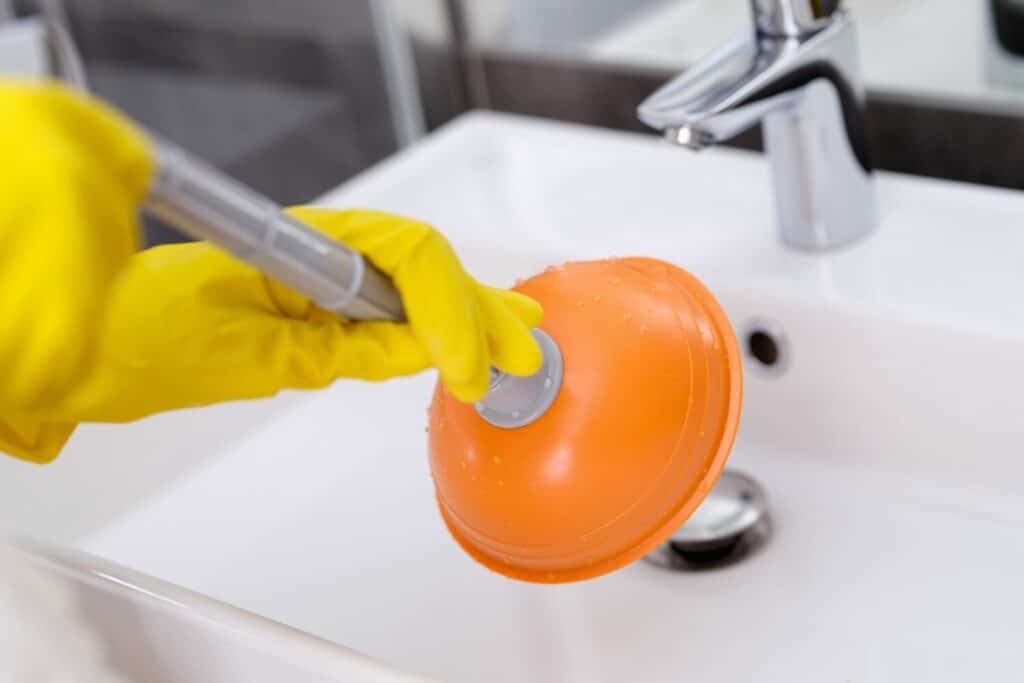 plumber with rubber gloves cleaning sink with plunger bathroom closeup 151013 26939