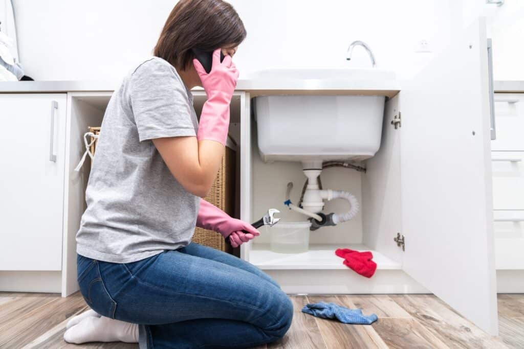 woman sitting near leaking sink laundry room calling help 130111 1682
