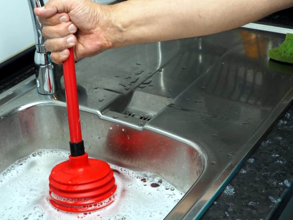 man cleans clogged kitchen sink with red plunger 543222 739